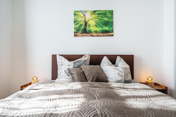 Ein Bett mit einer gesteppten Musterung, ein Baumgemälde und zwei Nachttischlampen.