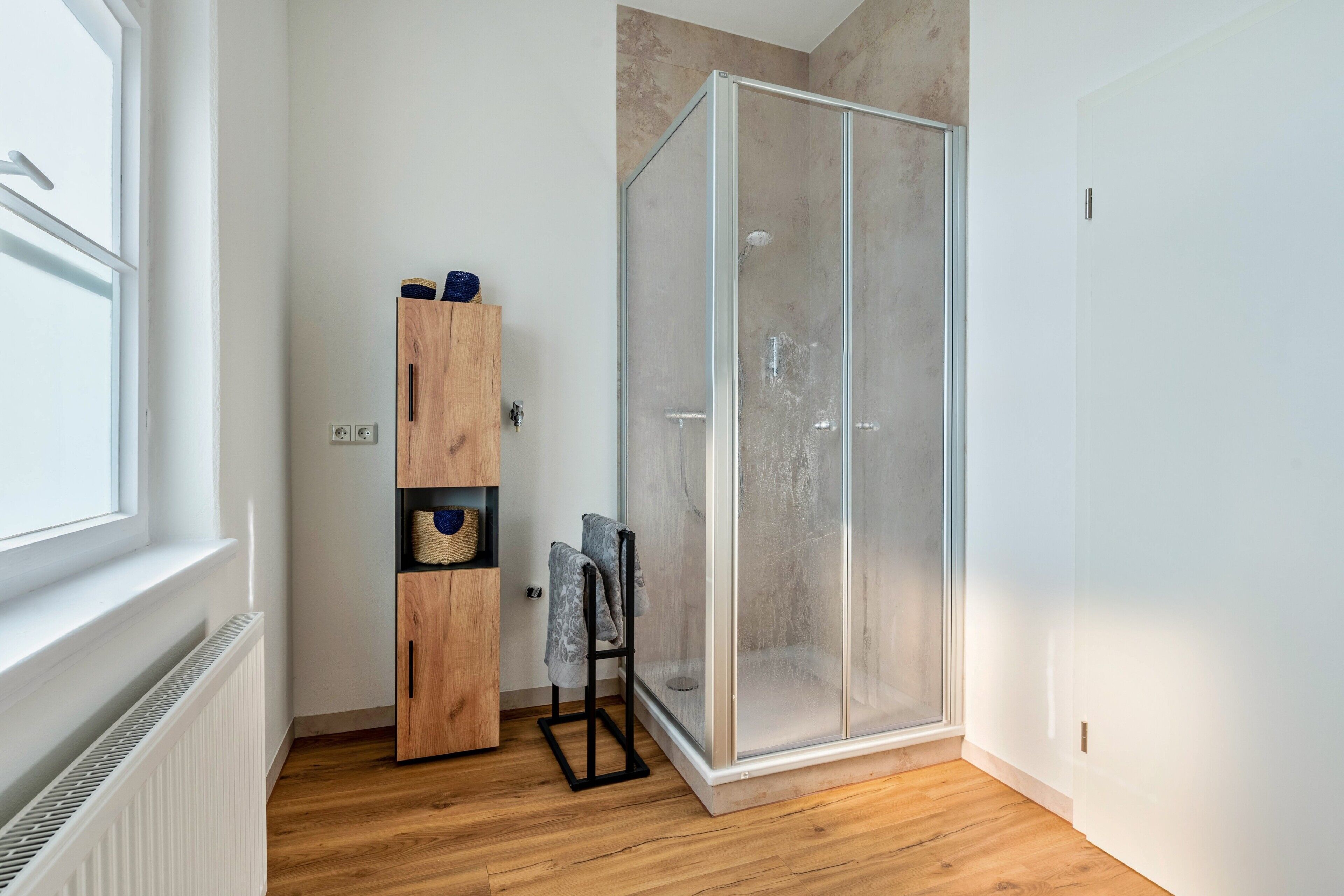 A modern bathroom with a glass shower enclosure, wooden cabinets, and a towel rack.