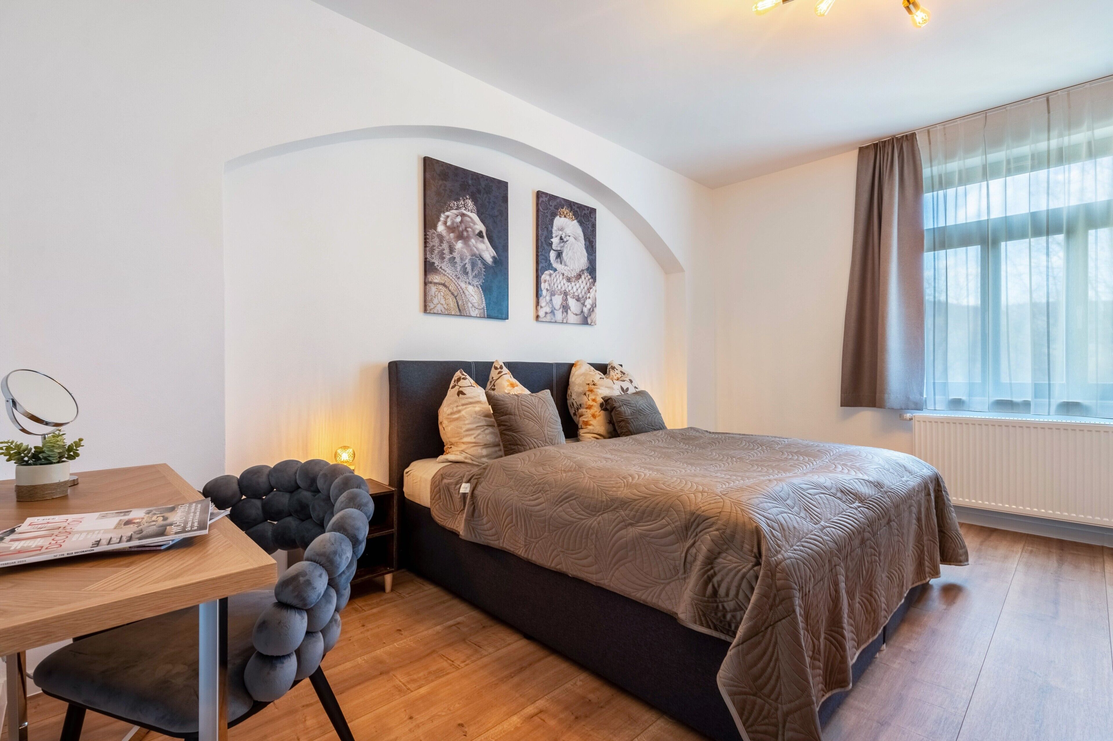 Ein Schlafzimmer mit einem Bett, einem Schreibtisch, einem Sessel und zwei an der Wand befestigten Kunstwerken.