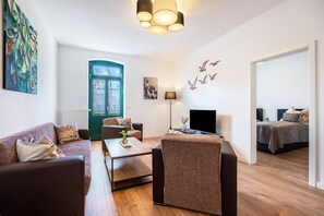 A modern living room with a sofa, armchair, coffee table, and a TV. - Apartment 6 with Private Terrace, Shared Garden and Wi-Fi (Rathmannsdorf)