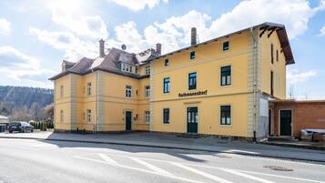 Ein gelbes Gebäude mit der Aufschrift 'Rathmannsdorf' an der Fassade, eine gepflasterte Straße davor und ein klarer Himmel.
