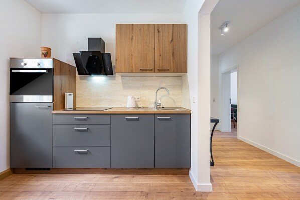 Une cuisine moderne avec des meubles gris, un plan de travail en bois et un four encastré.