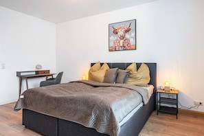 A bedroom with a bed, bedside table, lamp, and a desk with chair.