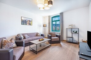 A modern living room with a sofa, armchairs, a coffee table, a TV, and a bookshelf.