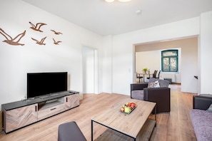 A modern living room with a flat-screen TV, wooden coffee table, and a dining area with a table and chairs.