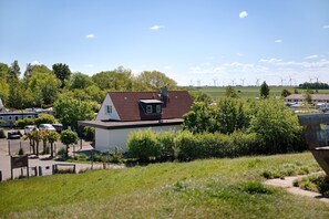 Ein Wohngebiet mit einem Haus, geparkten Autos und Windkraftanlagen im Hintergrund.