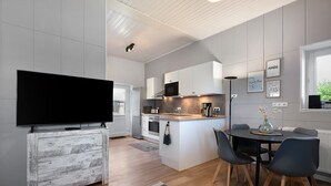A modern kitchen with a flat-screen TV, white cabinets, a coffee machine, and a dining area with a table and chairs.