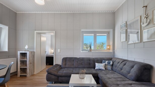A modern living room with a grey sectional sofa, a white coffee table, and a wooden bookshelf.