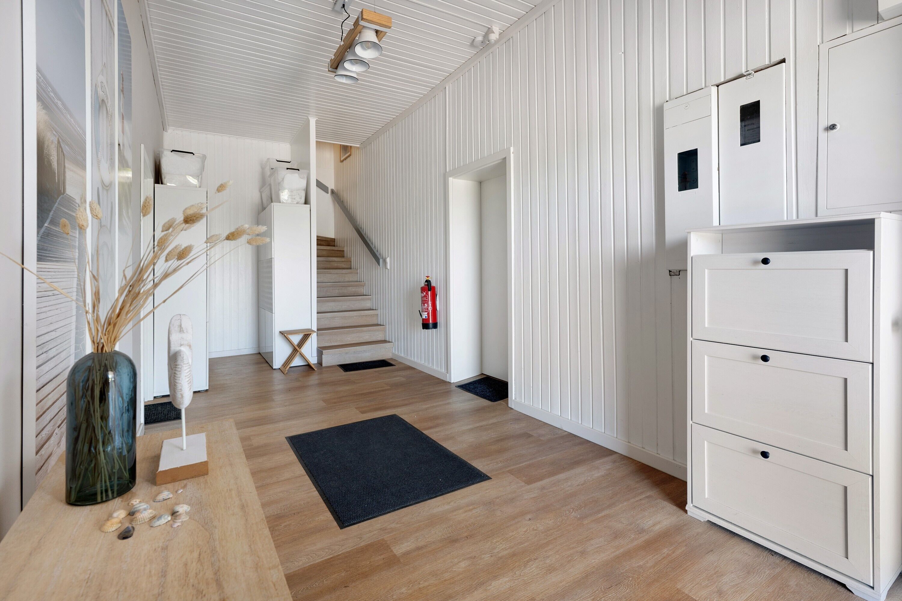 A hallway with wooden flooring, a black rug, a white cabinet, and a staircase.