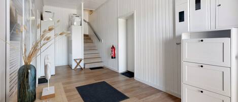 A hallway with wooden flooring, a black rug, a white cabinet, and a staircase.