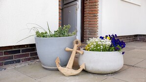 Trois plantes en pot, décorées d’une ancre, sur une terrasse carrelée.