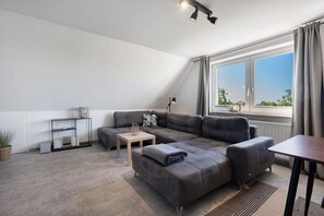 A modern living room with a sectional sofa, a small table, a floor lamp, and a view of the outdoors through a large window.