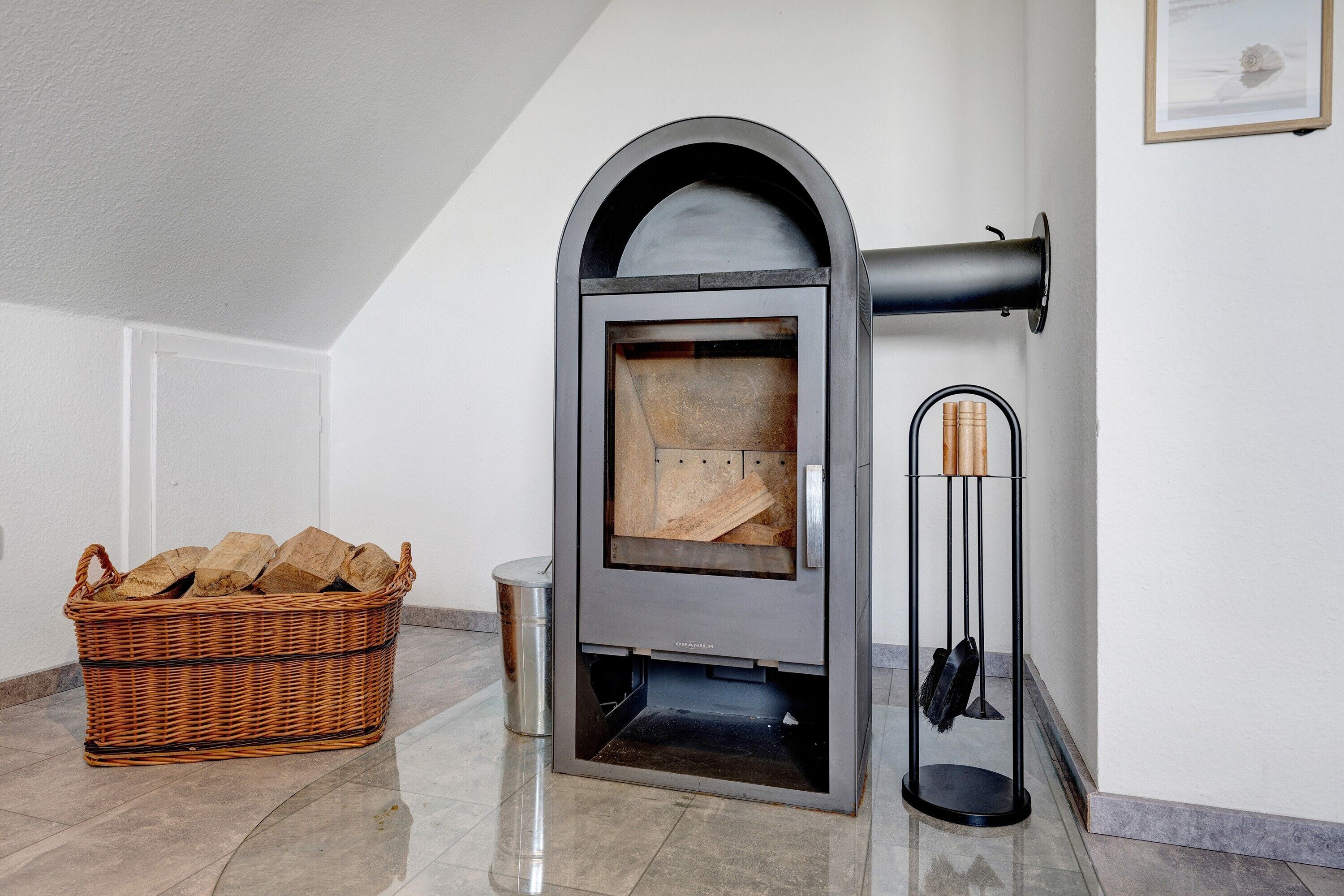 A modern fireplace with a basket of firewood, a metal container, and a coat rack.
