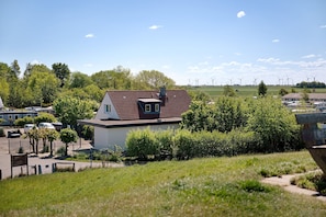 A residential area with a house, parked cars, and wind turbines in the background.