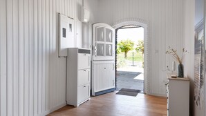 Un couloir aux murs en bois peints en blanc, avec une armoire blanche et une porte donnant sur l’extérieur.