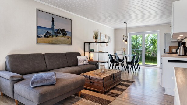 A modern living room with a sofa, coffee table, and a painting of a lighthouse. - Apartment 'Links' with Private Terrace and Private Garden (Wesselburenerkoog)