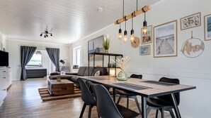 A modern living room with a dining area, wooden flooring, and a ceiling with exposed beams. - Apartment 'Links' with Private Terrace and Private Garden (Wesselburenerkoog)