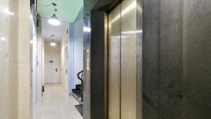 Um corredor com piso de azulejos, um elevador de metal e uma porta no final.