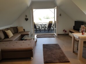 Een modern loft appartement met een bank, een eettafel, een televisie en een balkon met buitenmeubilair.