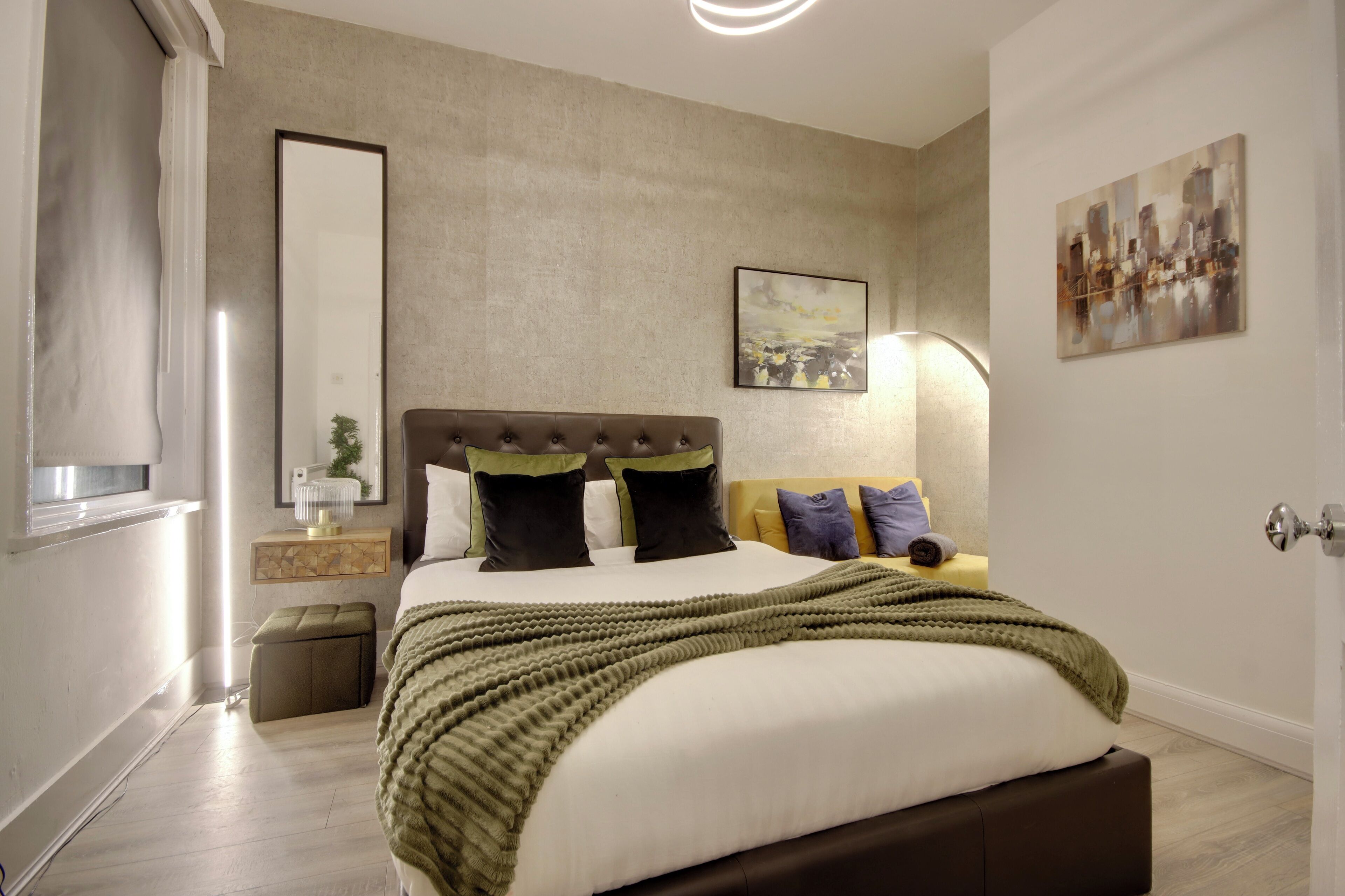 A modern bedroom with a large bed, a bedside table, a mirror, and artwork on the walls.