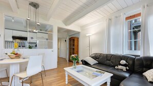 Een moderne woonkamer met een zwarte leren bank, een witte salontafel en een eethoek met een witte tafel en stoelen.
