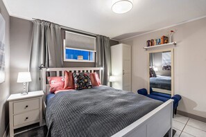 A bedroom with a bed, nightstands, a mirror, a window with curtains, and a bookshelf.
