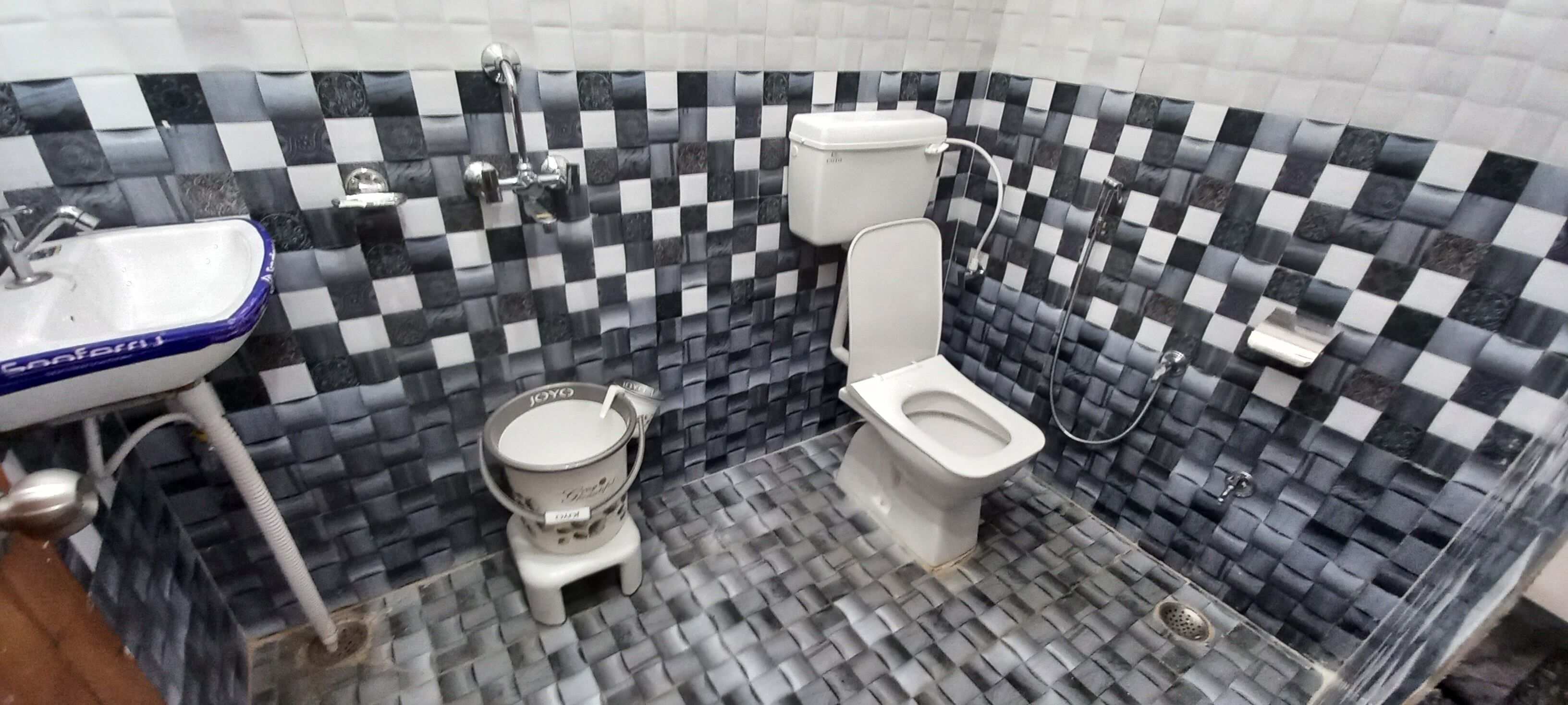 A bathroom with a checkered black and white tiled wall, a white sink, a toilet, and a bidet.