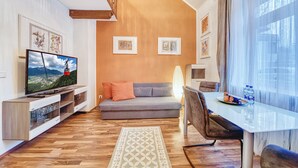 A modern living room with a flat-screen TV, grey sofa, wooden entertainment unit, and a dining table with chairs.