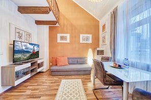 A modern living room with a flat-screen TV, grey sofa, wooden entertainment unit, and a dining table with chairs.