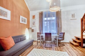 A modern living room with a grey sofa, a dining table with four chairs, a chandelier, and artwork on the walls.