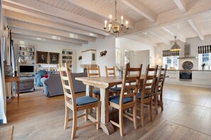 A spacious living area with a dining table, chairs, and a chandelier. There are bookshelves and a fireplace in the background. - Holiday Home 'Brunnenhaus' with Private Terrace, Garden and Wi-Fi (Walkendorf)