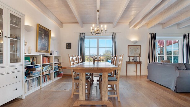 Una sala menjador amb taula de fusta, cadires, un penjallum, una prestatgeria i una vista per la finestra.