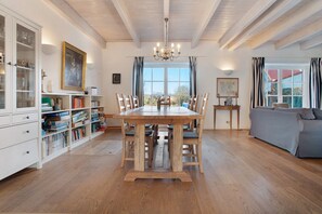Ein Esszimmer mit Holztisch, Stühlen, einer Chandelierleuchtre, einem Bücherregal und Blick durch ein Fenster.
