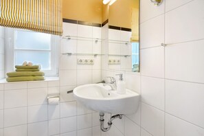 Une salle de bain avec un lavabo blanc, une fenêtre avec des serviettes et un miroir.
