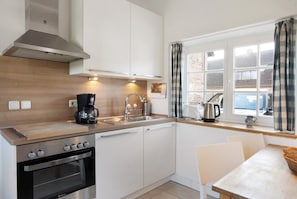A modern kitchen with a stove, oven, sink, and window with curtains.