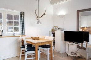 A dining area with a wooden table and chairs, a television on a stand, and a window with curtains.