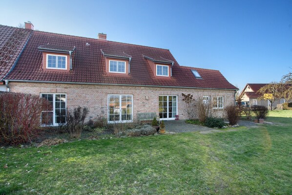 A two-story brick house with a red-tiled roof, large windows, and a well-maintained lawn.