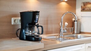 A modern kitchen with a black coffee maker, a stainless steel sink, and wooden cabinetry. - Holiday Apartment 'Jägerkate' with Private Terrace, Shared Garden and Wi-Fi (Walkendorf)