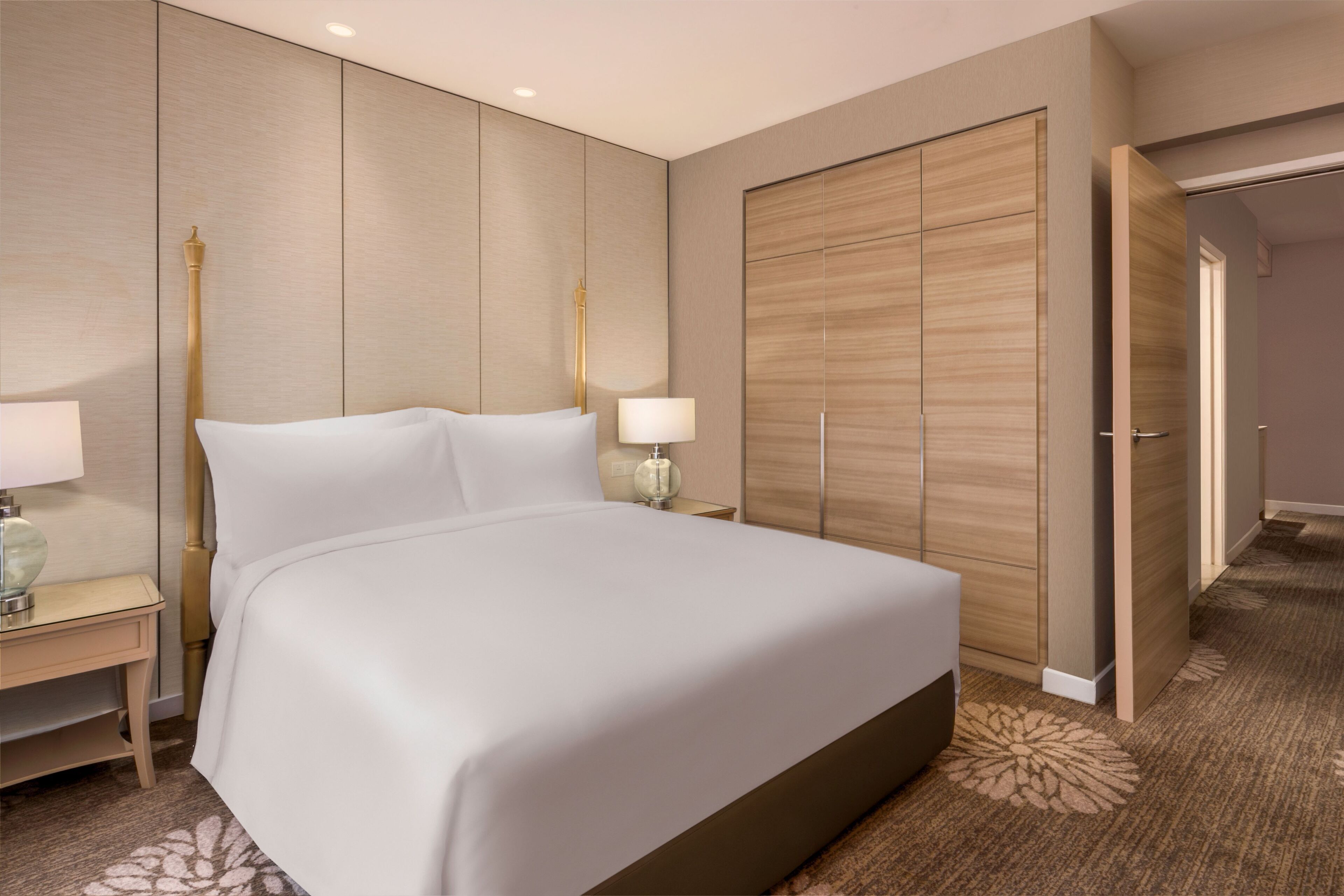 Habitación de hotel con una cama grande, mesitas de noche con lámparas, un armario y suelo alfombrado.