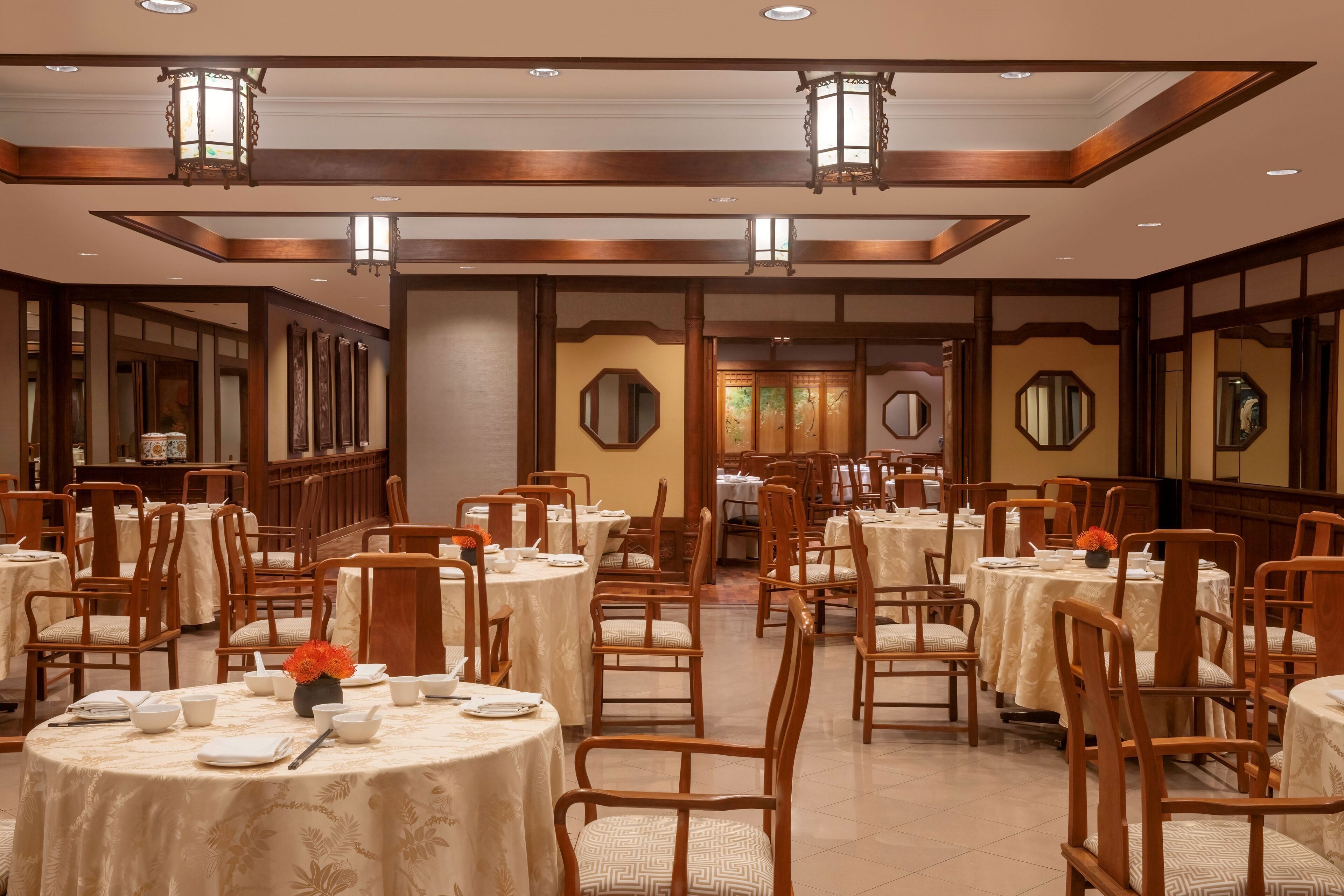 A dining area with round tables, wooden chairs, and traditional lanterns.
