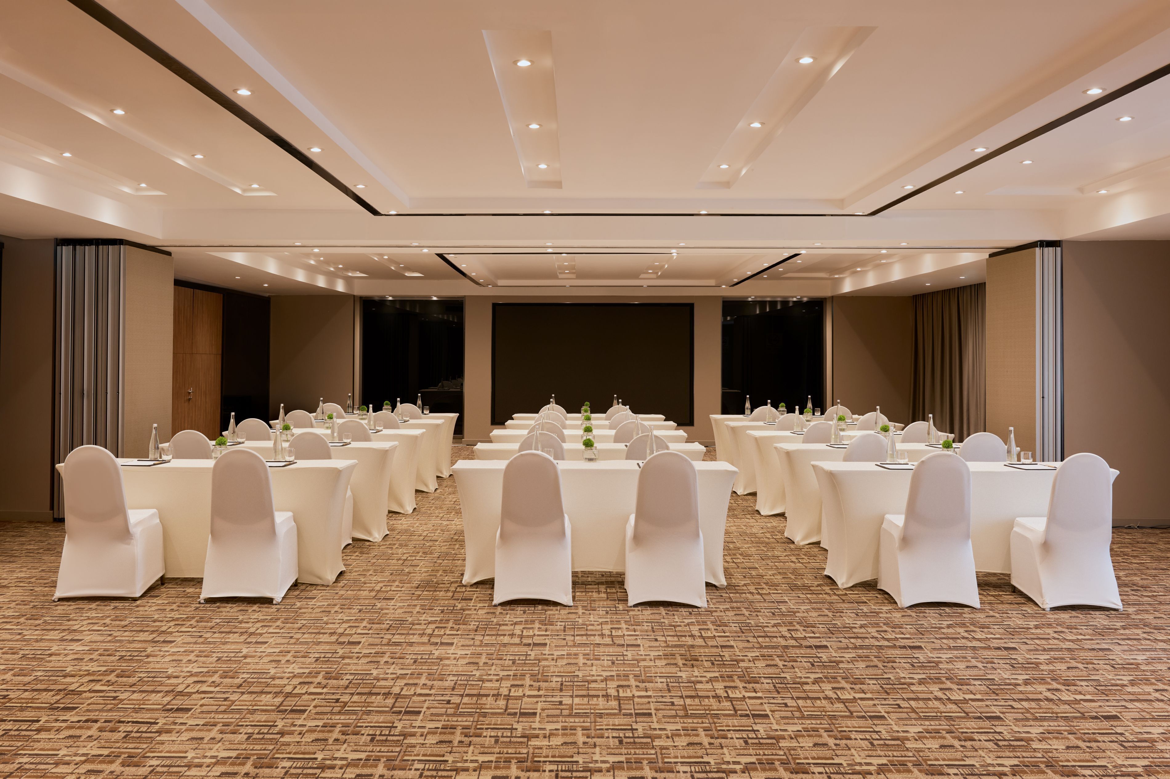 A conference room with multiple tables and chairs, carpeted floor, and recessed lighting.