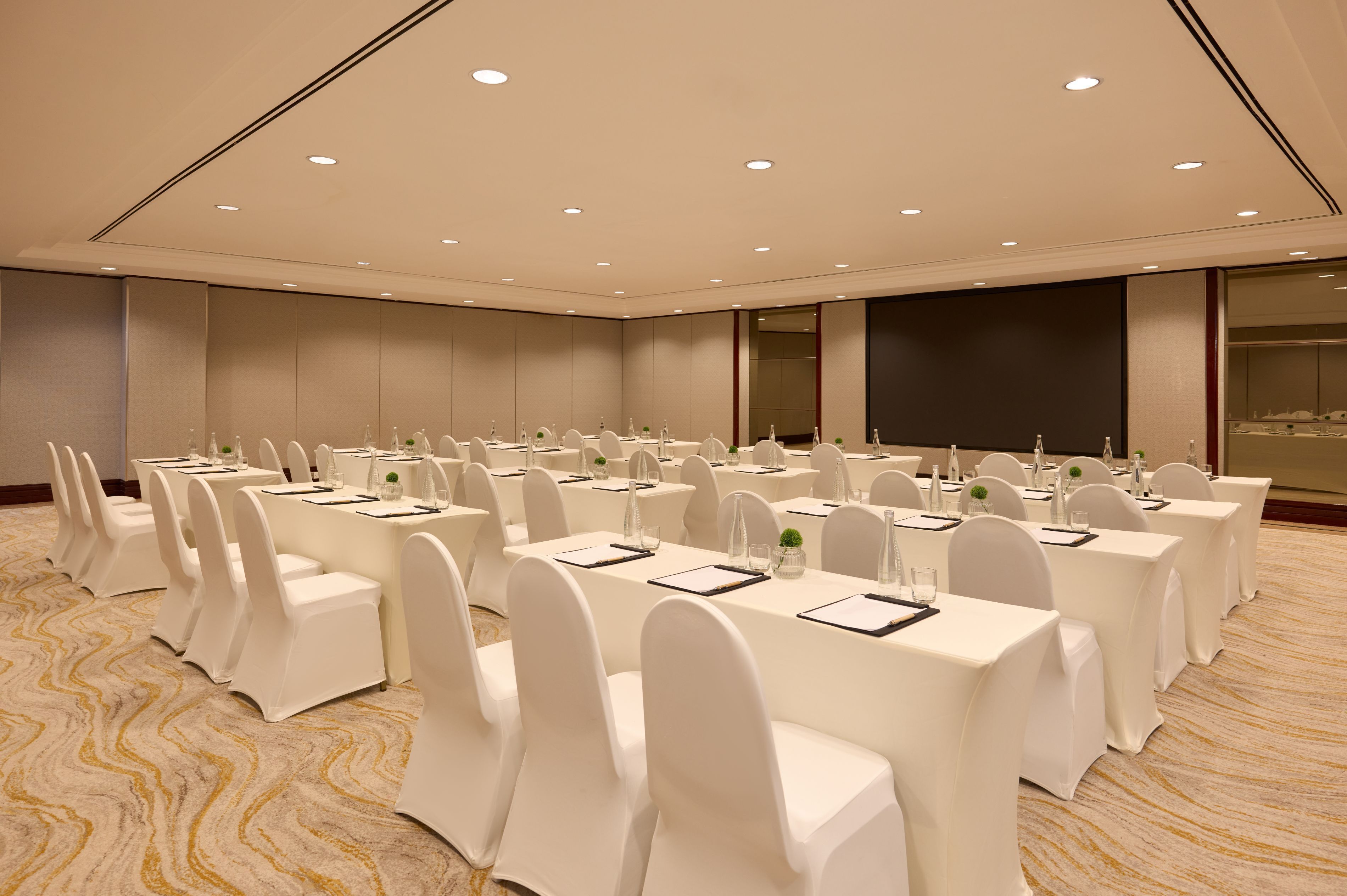 Une salle de conférence avec des rangées de tables et de chaises, équipée de plaques nominatives et de bouteilles d’eau.