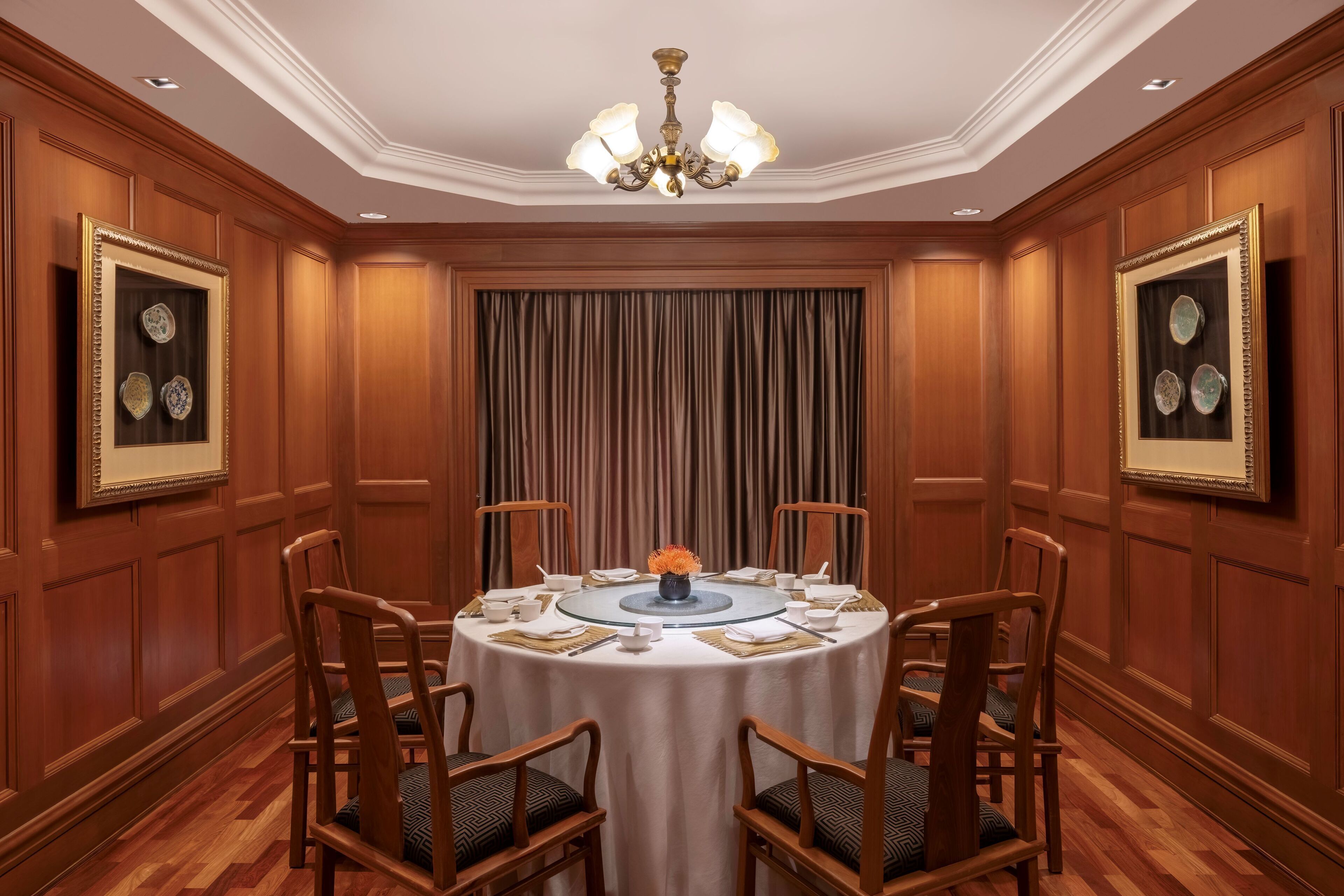 A formal dining room with a round table, wooden chairs, and a chandelier.
