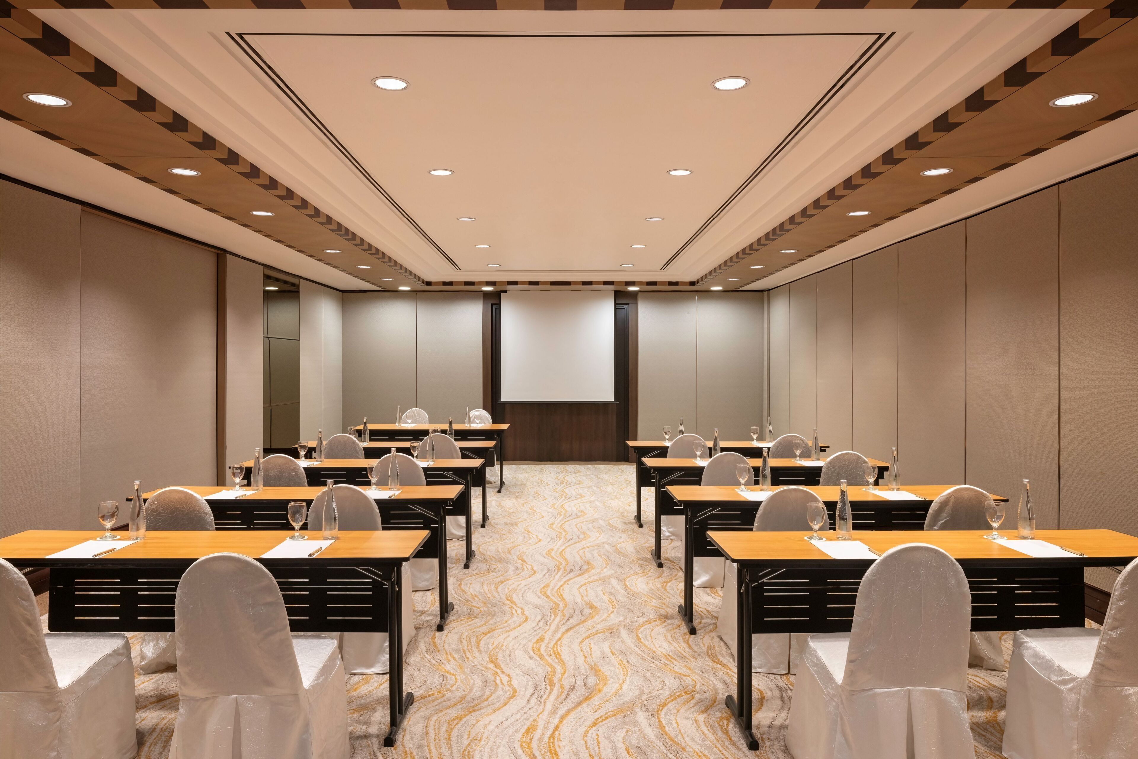 A conference room with a long table, chairs, and a projector screen.