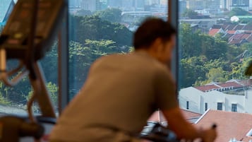 Una persona hace ejercicio en una bicicleta estática con vistas a la ciudad a través de amplias ventanas.