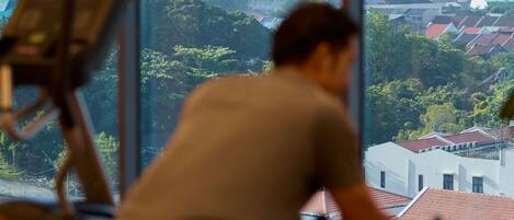 A person exercising on a stationary bike with a cityscape view through large windows.