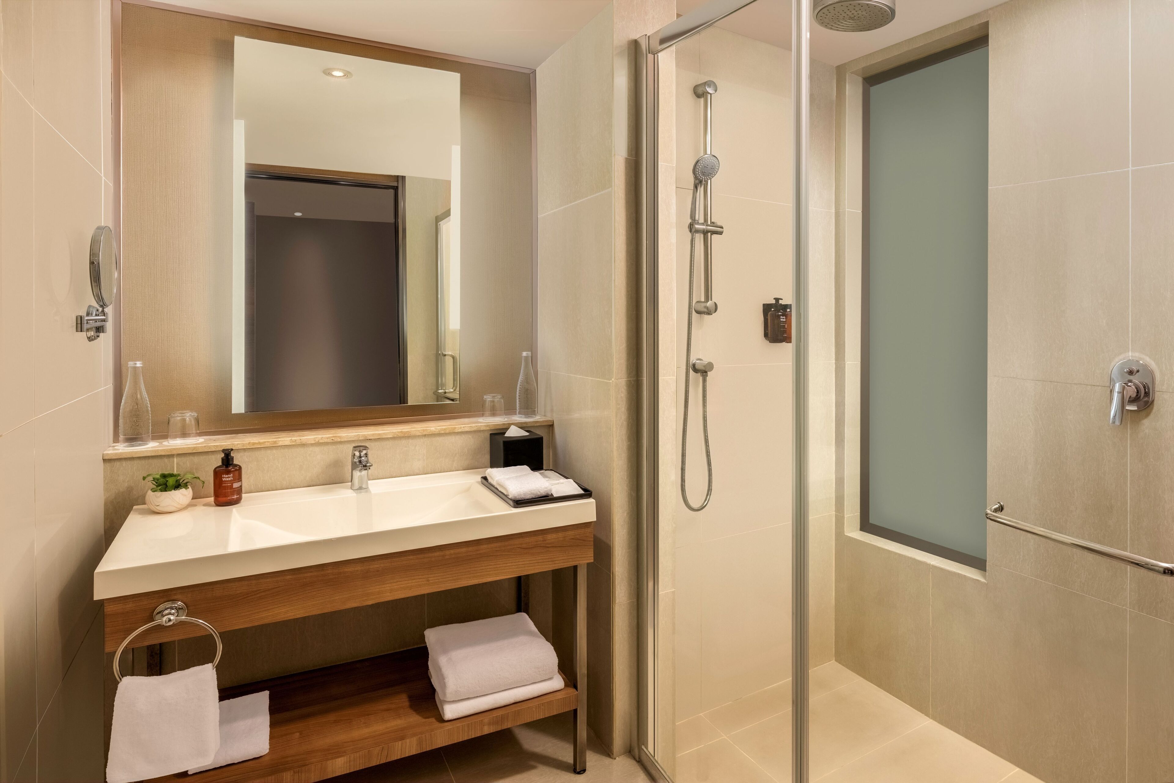 Ein modernes Badezimmer mit einer gläsernen Dusche, einem Holzwaschtisch mit Spiegel und einem Handtuchhalter.