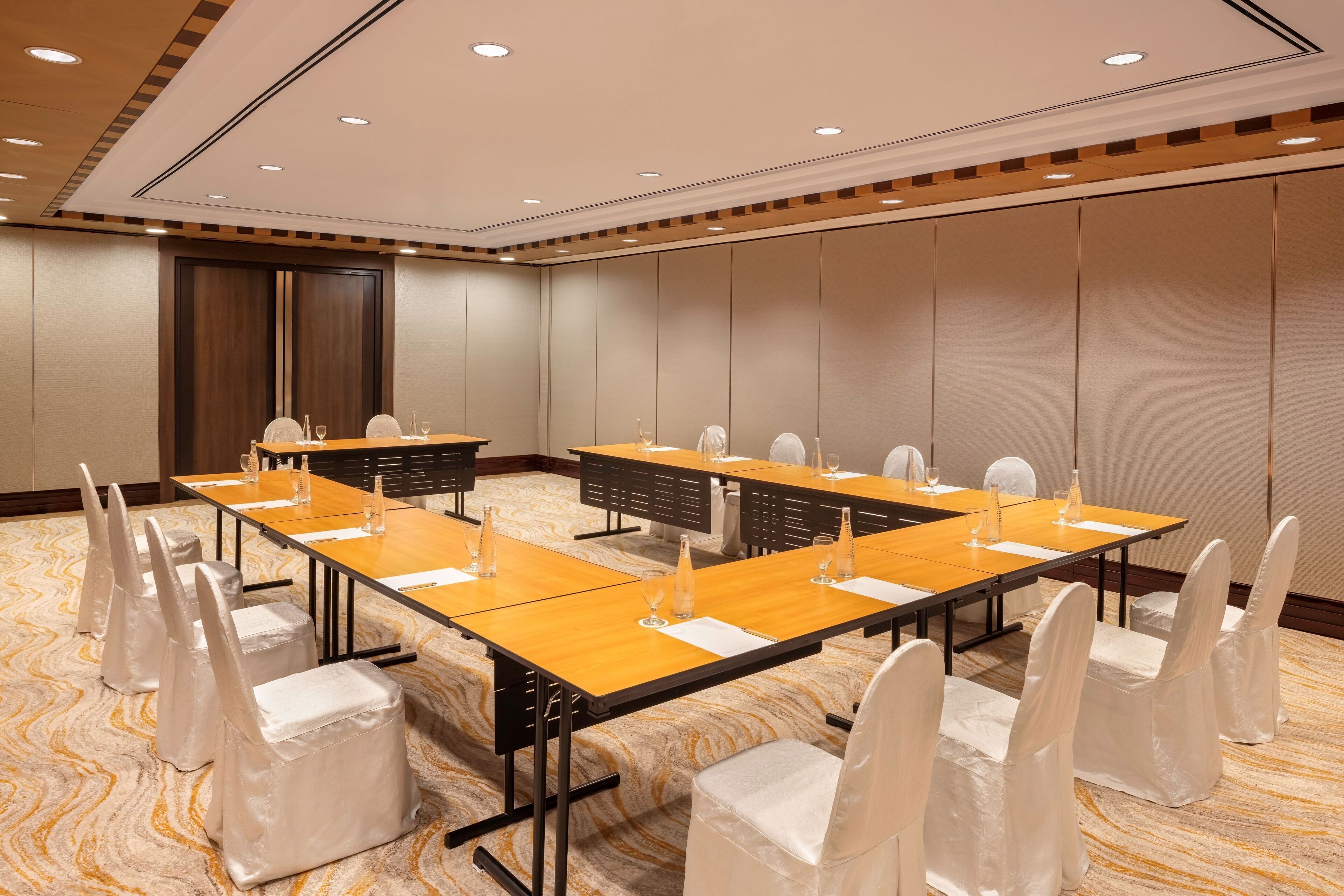 Une salle de conférence avec de longues tables, des chaises blanches et un tapis à motifs.