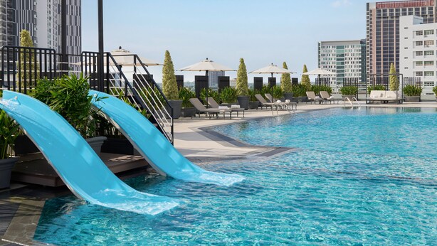 Ein Schwimmbecken mit Wasserrutschen, Liegestühlen und Sonnenschirmen.