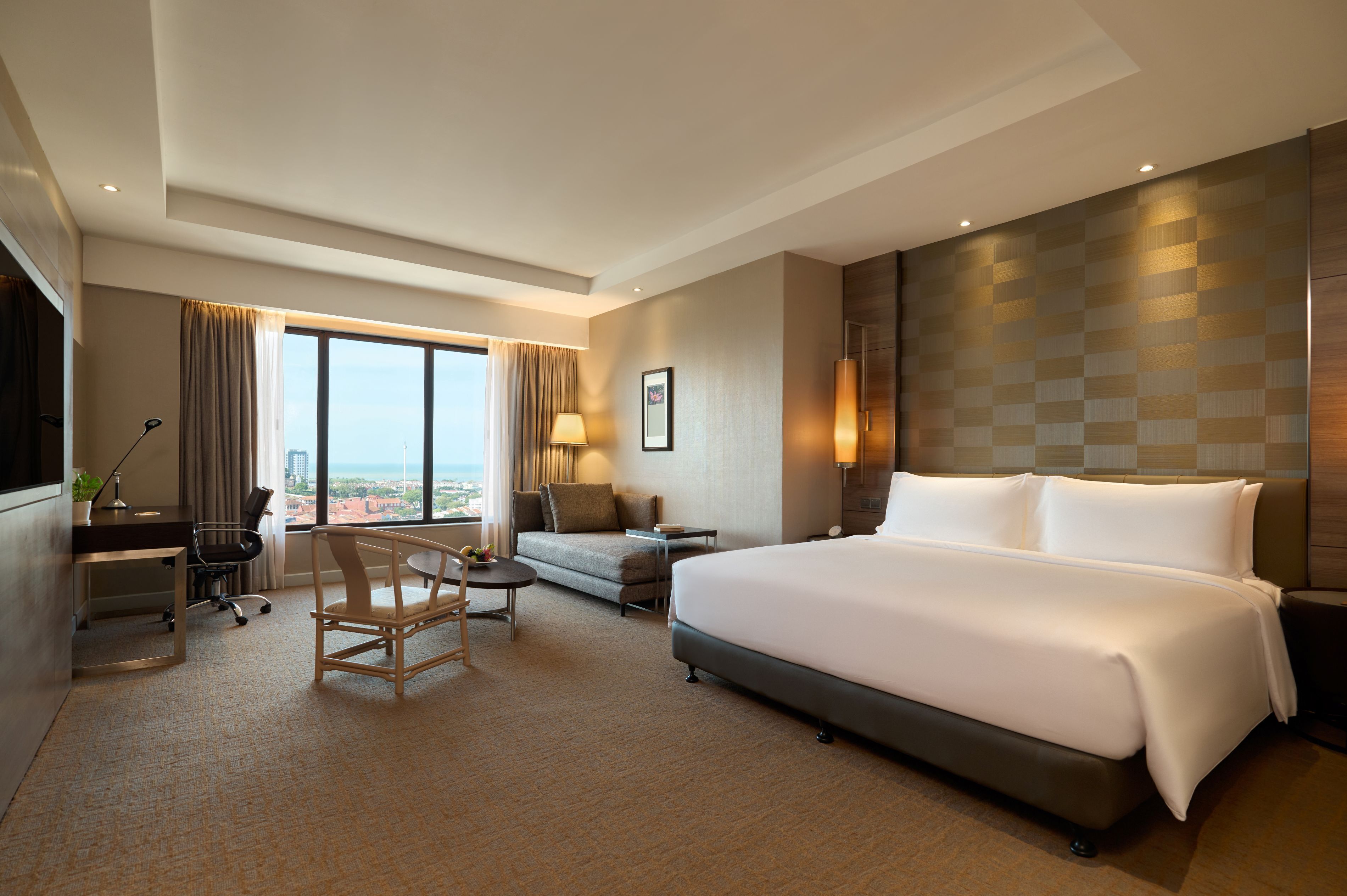 Een hotelkamer met een groot bed, een bureau, een stoel, een bank en uitzicht op de stad.